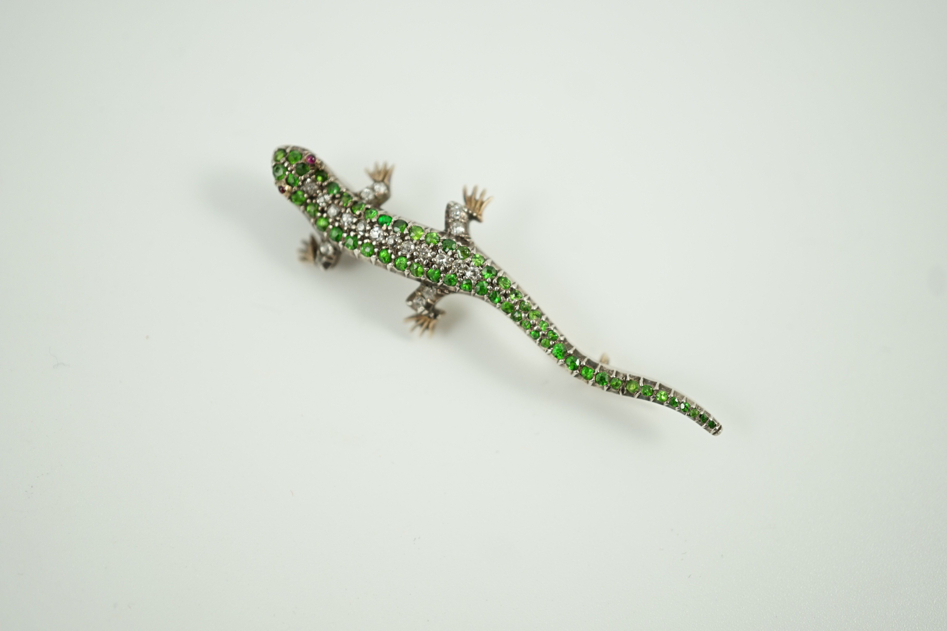 An Edwardian yellow metal, diamond and green garnet set lizard brooch, with red cabochon eyes, 50mm, gross weight 6.2 grams.